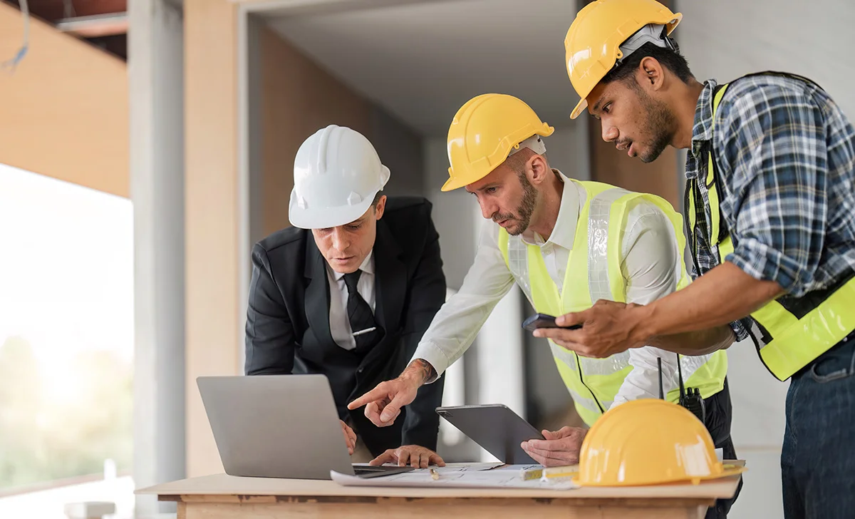 A commercial general contractor looks over plans for a construction project with team members wearing hard hats